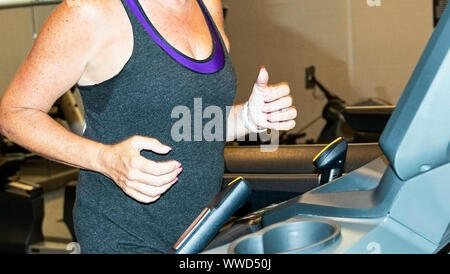 A women is running on a treadmill indoors in the hotel gym on vacation. Stock Photo