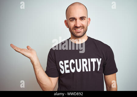 Young safeguard man wearing security uniform over isolated background smiling cheerful presenting and pointing with palm of hand looking at the camera Stock Photo