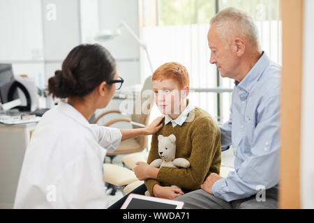 Back view portrait of caring nurse cheering up red haired boy during consultation in doctors office, copy space Stock Photo