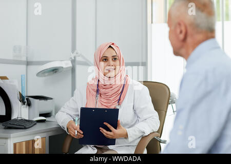 Portrait of young Arab woman working as nurse in medical clinic and talking to senior patient, copy space Stock Photo