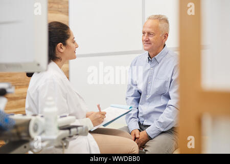 Portrait of friendly female doctor writing on clipboard while examining senior patient in medical clinic, copy space Stock Photo