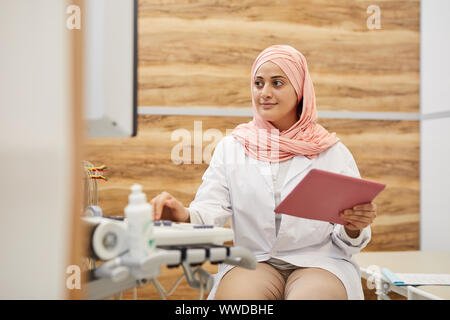 Portrait of young Arab woman using electronic machines while working as nurse in medical clinic, copy space Stock Photo