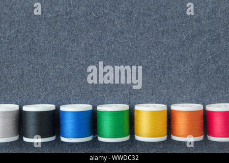 Row of spools of multicolored threads on sewing cloth. View from above. Copy space for text. Stock Photo