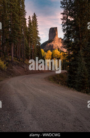 Beautiful light hitting Chimney Rock near Ridgway, Colorado during the autumn.  Golden aspens. Fall Colors. Gravel forest road leads to the scene. Stock Photo