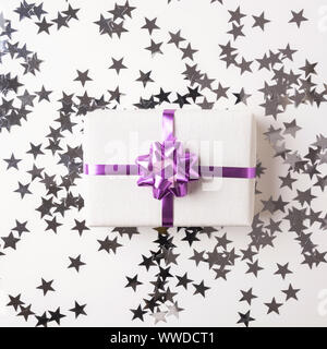 Christmas gift box with violet bow on white table with silver sparkling star. Xmas background. Flat lay. Top view. Stock Photo