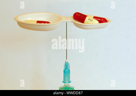 Medicine spoon balanced, yes really balanced, on a needle, containing Amoxicillin capsules Stock Photo