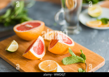 Delicious fresh citrus fruit lemon, grapefruit, lime with green mint leaves on gray background, closeup. Mojito, lemonade, vitamins, summer concept Stock Photo