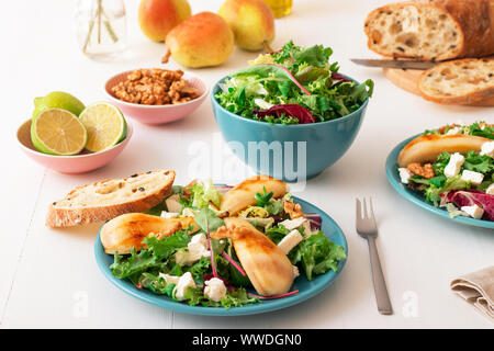 White wooden table with walnut salad, caramelised pears and feta cheese. Turquise dishes with salad, slices of twisted swiss bread with olives, limets Stock Photo