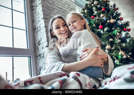 Mother and her daughter sitting together near christmas tree Stock ...