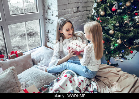 Merry Christmas and Happy Holidays! Cheerful mom and her cute daughter girl exchanging gifts. Parent and little child having fun near Christmas tree i Stock Photo