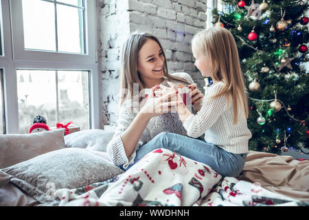 holidays, presents, christmas, x-mas, birthday concept - happy mother and child girl with gift box near Xmas tree. Morning Xmas Stock Photo