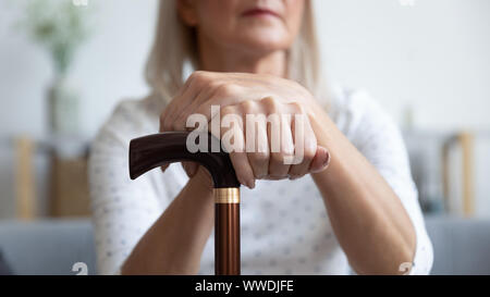 Serious older woman holding hands on wooden cane close up Stock Photo