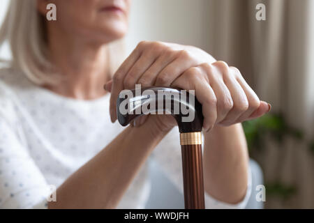 Mature woman holding hands on cane close up, sitting alone Stock Photo