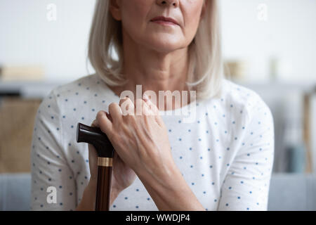 Unhappy mature woman holding hands on walking stick close up Stock Photo
