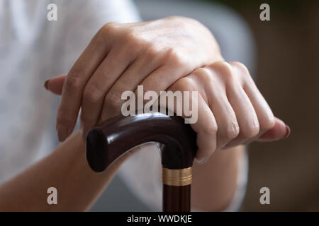 Older woman holding hands on wooden walking stick close up Stock Photo