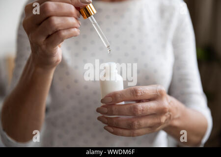 Close up mature woman dropping collagen moisturizer face serum Stock Photo