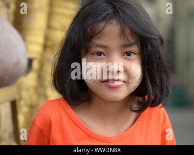 Cute little Burmese girl with patches of yellowish-white traditional thanaka face cosmetic on her cheeks and nose smiles for the camera. Stock Photo