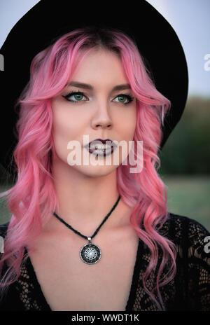 Halloween theme: beautiful young pink-haired witch in black dress and hat. Close-up portrait Stock Photo