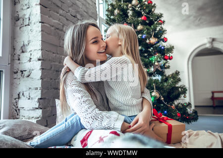 Family, holidays and happiness concept - happy daughter kissing her mother over christmas tree lights background. Winter holiday Xmas and New Year con