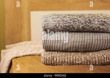 A pile of knitted winter or autumn sweaters on the wood bed. Warm comfortable clothes. Stock Photo