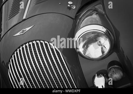 Front detail of a red Morgan sports car showing badge, radiator grille, headlight and indicator light. Stock Photo