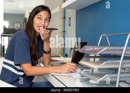 Woman taking a hands-free call and working on some blueprints at the office Stock Photo