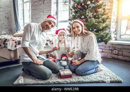 Family celebrating at home. father, mother and children on the background of the Christmas tree with presents sit on the carpet. New Year and xmas peo Stock Photo