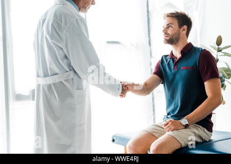 cropped view of doctor in white coat shaking hands with handsome man Stock Photo
