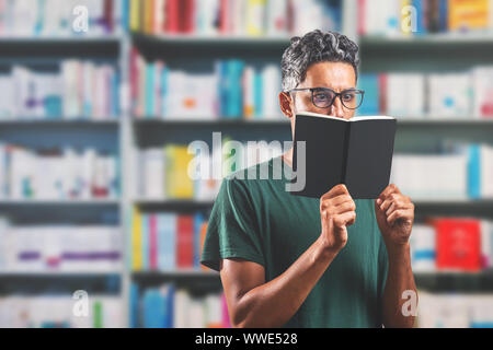 man wearing glasses reading a book in the library - shallow depth of field - blank book - space for text Stock Photo