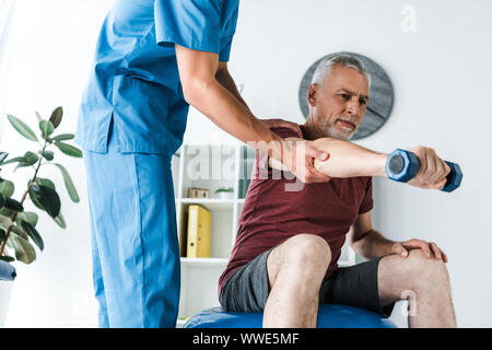 mature man training with dumbbell near doctor standing in clinic Stock Photo