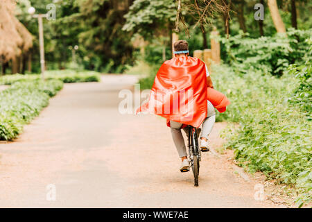 back view of father and son riding bicycle in red cloaks Stock Photo