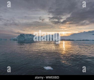 Arctic nature landscape with icebergs in Greenland icefjord with midnight sun sunset / sunrise in the horizon. Early morning summer alpenglow during Stock Photo