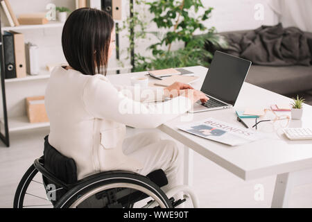 young disabled businesswoman using laptop while sitting in wheelchair at workplace Stock Photo