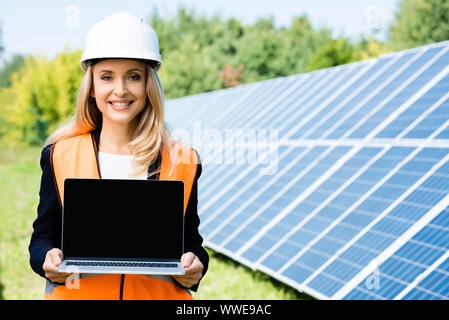 attractive businesswoman in hardhat and safety vest holding laptop with copy space Stock Photo