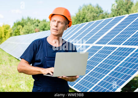 handsome engineer in t-shirt and orange hardhat holding laptop Stock Photo