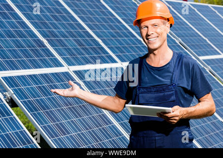handsome engineer in t-shirt and orange hardhat smiling and holding digital tablet Stock Photo