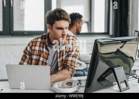 selective focus of thoughtful programmer working near african american colleague in office Stock Photo