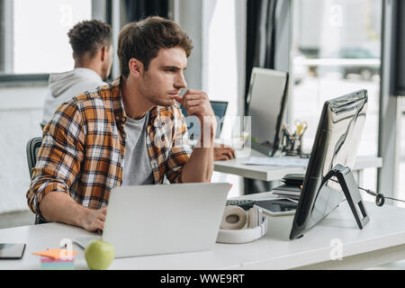 selective focus of serious programmer working near african american colleague in office Stock Photo