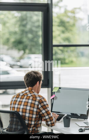 back view of young programmer sitting at workplace near window Stock Photo