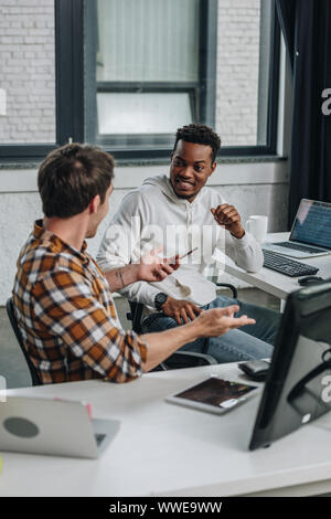 two cheerful multicultural programmers discussing ideas while sitting together in office Stock Photo