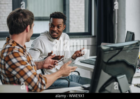 two excited multicultural programmers gesturing while talking in office Stock Photo