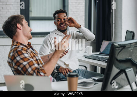 two cheerful multicultural programmers looking at each other while working in office together Stock Photo