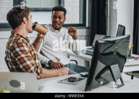 two young multicultural programmers talking while sitting together in office Stock Photo