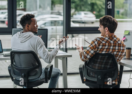 two young multicultural programmers gesturing while talking in office Stock Photo