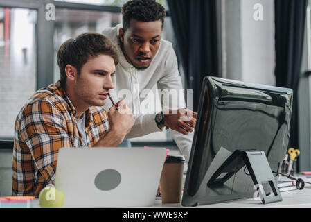 african american programmer pointing at computer monitor near serious colleague Stock Photo
