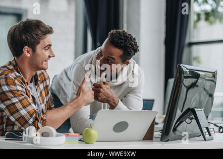 two happy multicultural programmers looking at each other and showing thumbs up Stock Photo