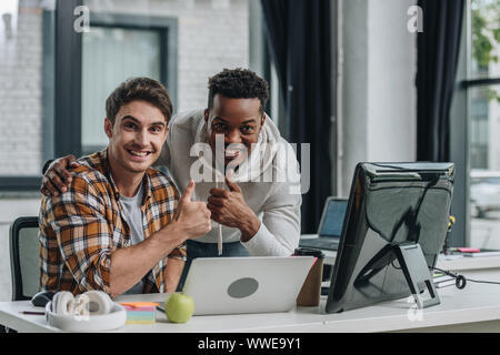 two young multicultural programmers smiling at camera and showing thumbs up Stock Photo