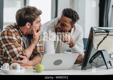 two shocked multicultural programmers looking at each other while working in office together Stock Photo