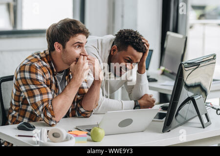 two shocked multicultural programmers looking at laptop in office Stock Photo