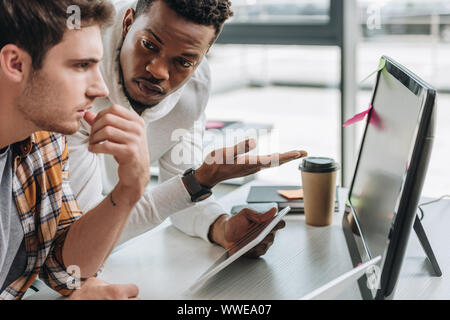 serious african american programmer pointing at computer monitor near colleague Stock Photo